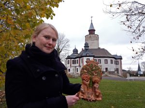 Franziska Huberty aus dem Museum Burg Posterstein hält eine spanische Tonkrippe in der Hand. Sie steht vorm Museum Burg Posterstein.