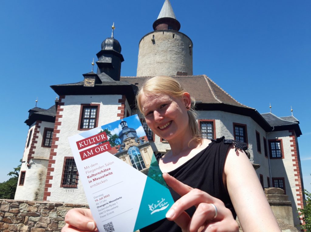 Franziska Huberty aus dem Museum Burg Posterstein mit einem Flyer von "Kultur am Ort" vor der Burg Posterstein