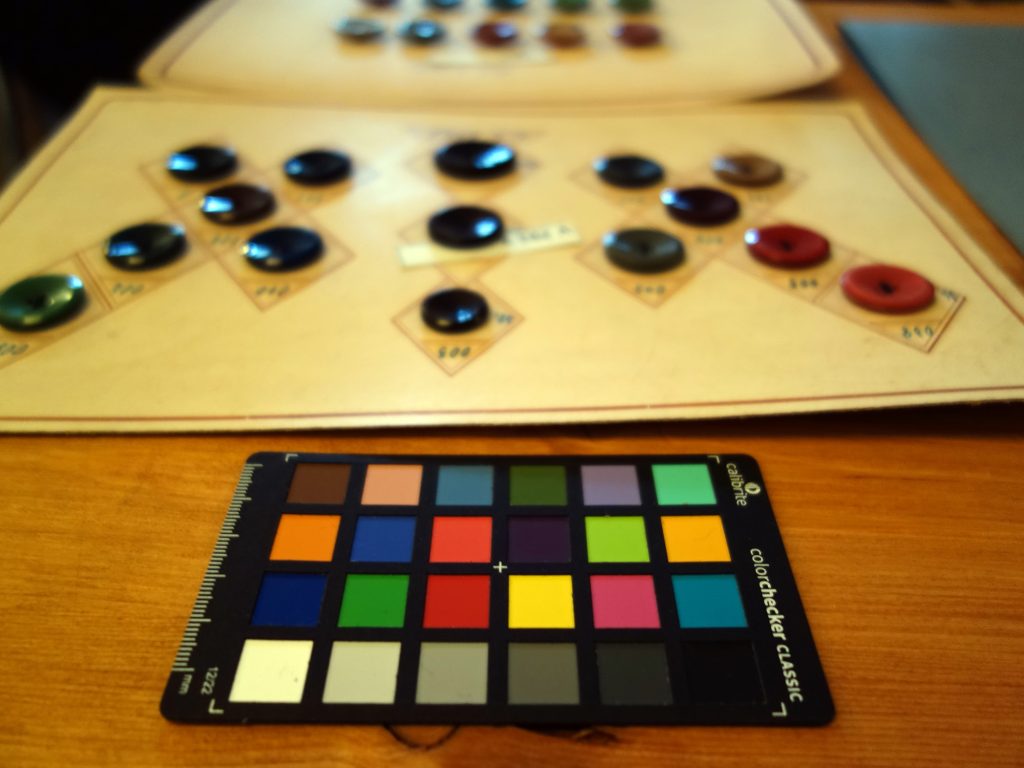 Eine Farbkarte, dahinter verschwommen Musterknopfkarten aus Schmöllner Knopffabriken