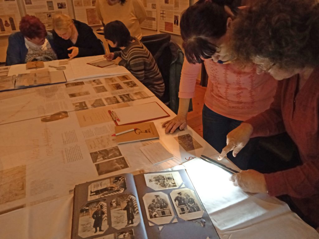 Fünf Menschen beugen sich mit Lupen über Postkarten in der Ausstellung auf Burg Posterstein
