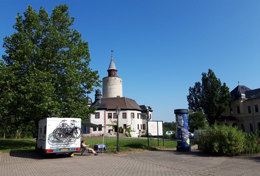 Wohnwagen vor der Burg Posterstein, eine Frau sitzt am Campingtisch und liest