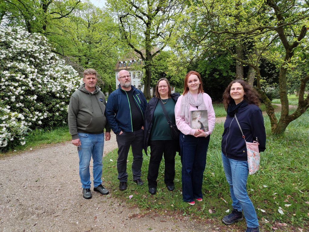 Fünf Menschen stehen im Schlosspark Tannenfeld, im Hintergrund blühen Rhododendren