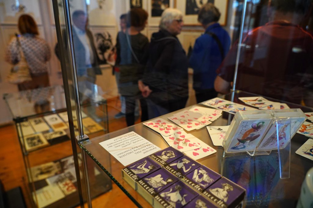 Im Vordergrund liegen Spielkarten und Streichholzschachteln in einer Vitrine, im Hintergrund Besuchende